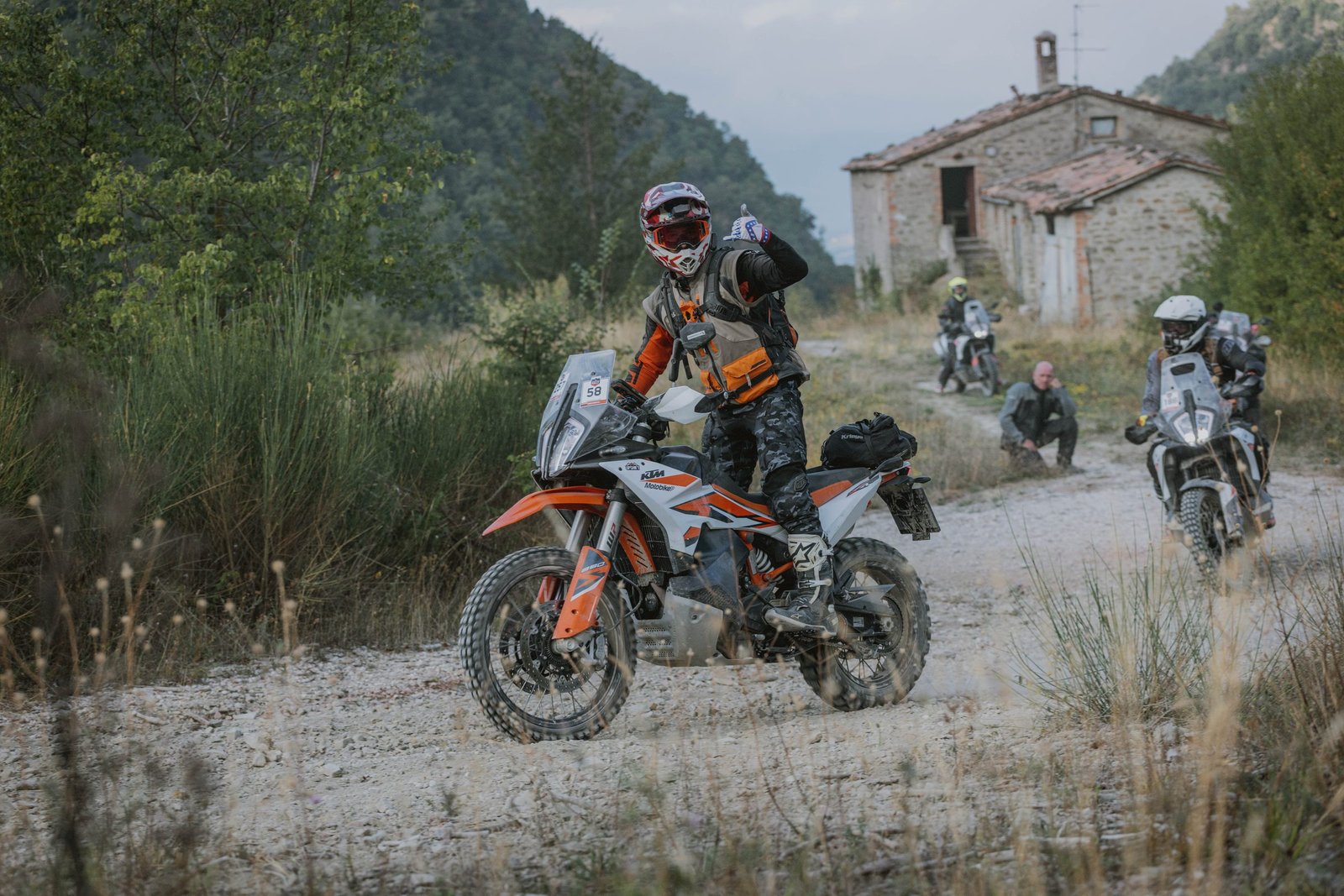 KTM rider on gravel past an old stone farmhouse, Umbria