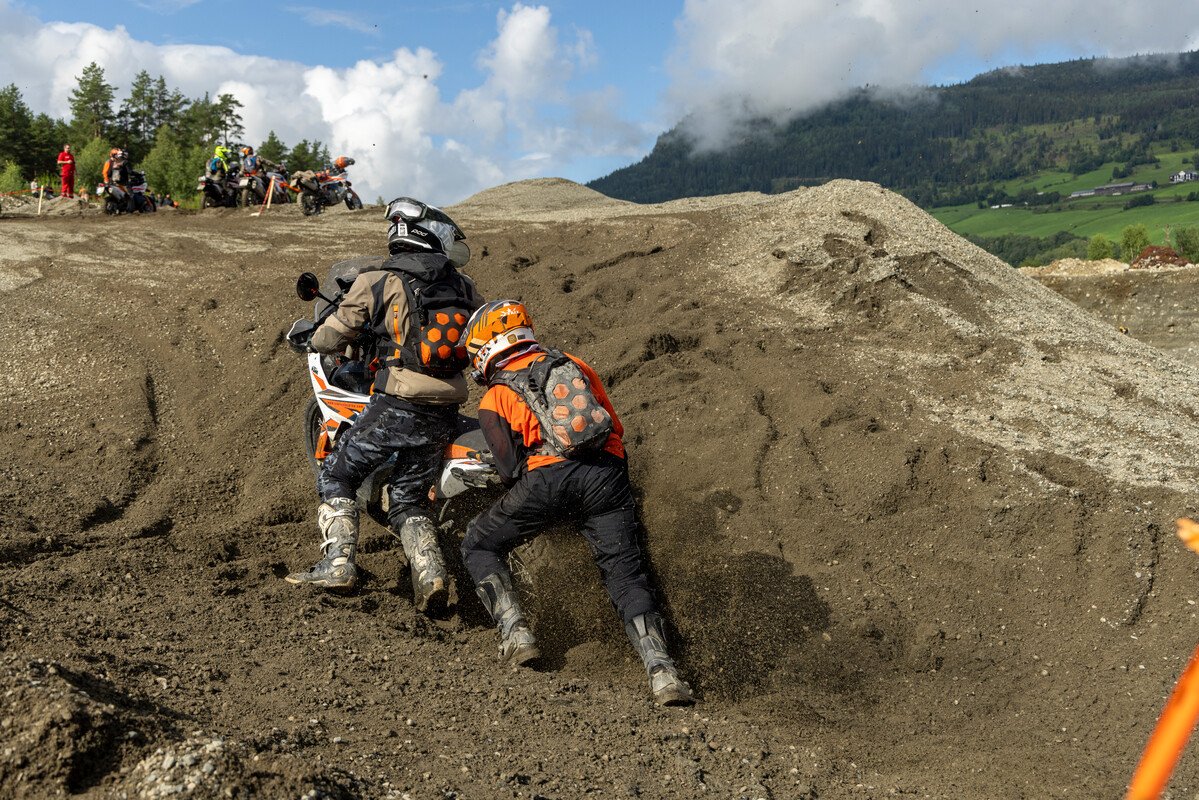 Riders pushing their KTMs up a steep technical slope