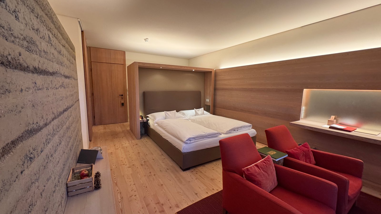 Vigilius Mountain Resort deluxe room with red armchairs, stone wall, and larch floor